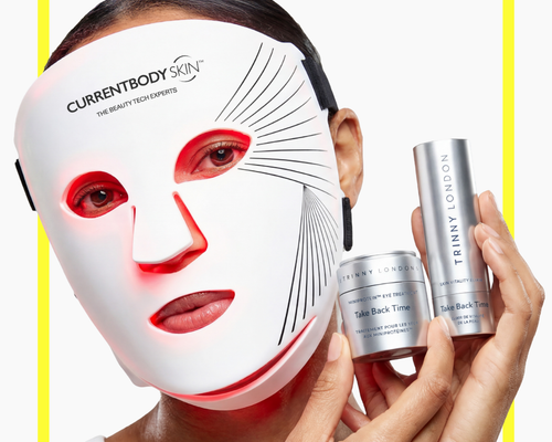 Woman wearing the Series 2 Red Light Mask and holding Trinny London products