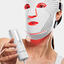 Woman wearing the CurrentBody Red Light LED Face Mask Series 2 and holding it's controller